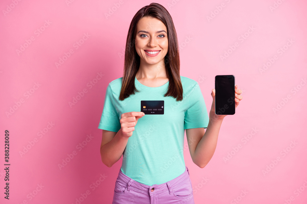Photo portrait of woman holding phone with blank space credit card isolated on pastel pink colored background - obrazy, fototapety, plakaty 