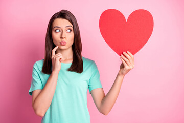 Poster - Photo portrait of cute girl sending air kiss pouted lips keeping red heart looking at copyspace isolated on pastel pink color background