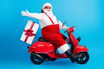 Wall Mural - Full length profile photo of grandfather grey beard ride motorcycle deliver present raise hand wear santa x-mas costume suspenders sunglass white shirt cap isolated blue color background