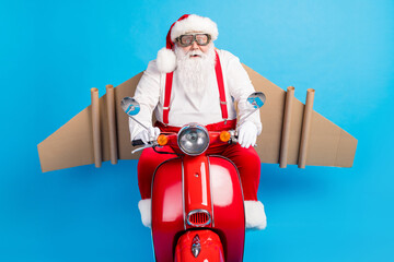 Sticker - Photo of funny crazy santa claus ride scooter fast speed with cardboard craft wings fly in sky wear modern stylish suspenders overalls glasses goggles cap isolated blue color background