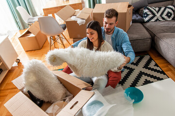 Wall Mural - Smiling young couple move into a new home sitting on floor and unpacking boxes of their belongings.