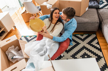 Wall Mural - Smiling young couple move into a new home sitting on floor and unpacking boxes of their belongings.