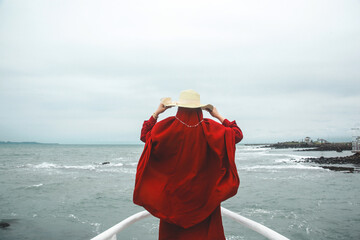 back side of woman with red scarf and holding summer hat standing on the front of the boat deck looking at the sea, vacations lifestyle concept