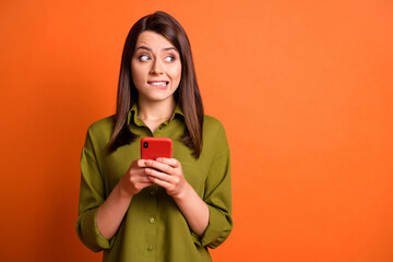 Wall Mural - photo of guilty young girl hold smartphone bite lip look side empty space wear green shirt isolated 