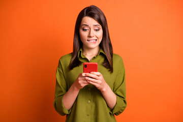 Wall Mural - photo of scared young girl hold telephone bite lip look screen wear green shirt isolated orange colo