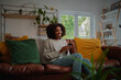 © StratfordProductions - Positive woman using smartphone while sitting at home looking away
