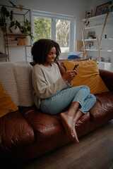 Beautiful african female watching video on smartphone at home while relaxing on couch