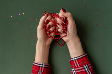 Christmas Manicure. Red Nails, Hands In Checkered Shirt Hold Red Beads On Green Background With Red Stars.