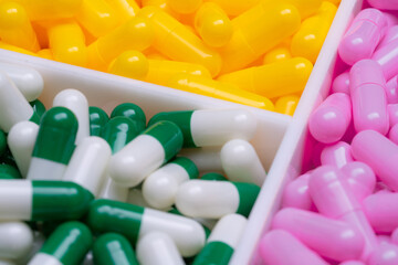 Sticker - Selective focus on capsule pills in plastic box. Pharmaceutical industry. Pink, yellow, and green-white capsule pills. Vitamins and supplements concept. Bright colors capsule in tray. Healthcare.