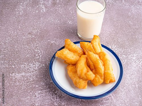 Cuadros en Lienzo Top view of deep-fried dough sticks or Chinese doughnut sticks on a white plate and a glass of soybean milk on gray stone background