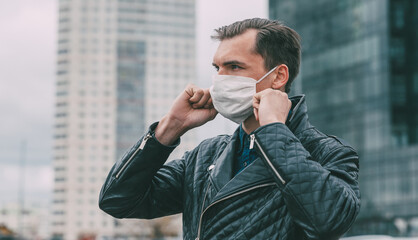 Wall Mural - young man putting on a protective mask standing on the street