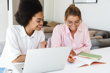 Wall Mural - Joyful multicultural students girls doing homework with laptop