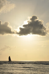 Wall Mural - Yellow sunset with cloud in front of the sun and horizon over water with a a sailing boat