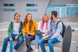 © damianobuffo - Multiethnic students joking and talking sitting on the bench together outdoors in a university - Group of happy young teenagers studying with books and tablets