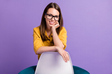 Poster - Photo of charming girl sit chair beaming toothy smile wear yellow shirt blue trousers glasses isolated violet color background