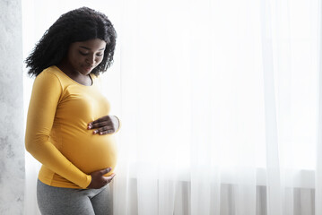 Beautiful pregnant african woman hugging her tummy at home