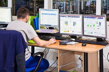 ULYANOVSK, RUSSIA - SEPTEMBER 6, 2016: A man in uniform sitting backwards at the desk with three displays and keyboards, controlling and monitoring the process of production.