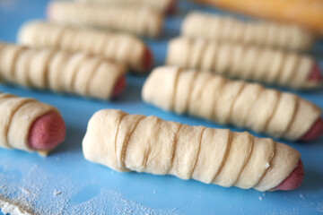 Blanks for fried pies. The sausages are wrapped in thin strips of yeast dough. The dough is rising. Copy space, selective focus