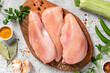 Raw uncooked chicken fillet on a wooden cutting board top view. Raw poultry fillet on a grey concrete background.