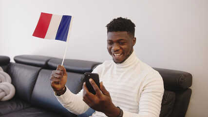 Young black man watching game play on smartphone and waving flag of France. High quality photo