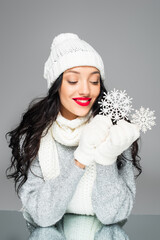 happy woman in winter outfit holding decorative snowflakes isolated on grey