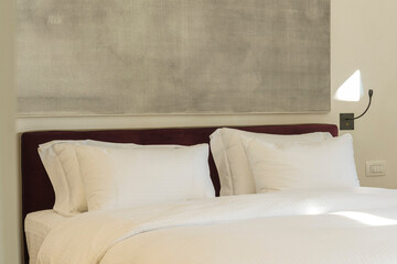 Details of the bedroom interior in light colors close-up - a fragment of a bed with two large white pillows, a lamp with a night light and a bedside table