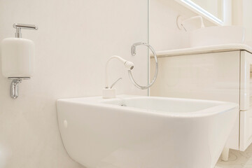 Close-up of a metal faucet with a white sink in a bathroom tiled with light tiles