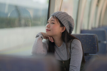 Poster - lifestyle portrait of young happy and beautiful Asian Korean woman excited and cheerful looking through window sitting on train enjoying landscape from the railcar glass