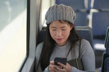 Canvas Print - lifestyle portrait of young beautiful and attractive Asian Chinese woman in winter hat sitting by window on train using internet mobile phone in transportation concept