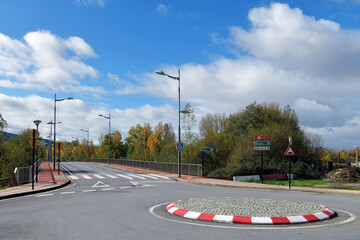 View of traffic circle or roundabout and empty paved road lined with street lamps and trees.