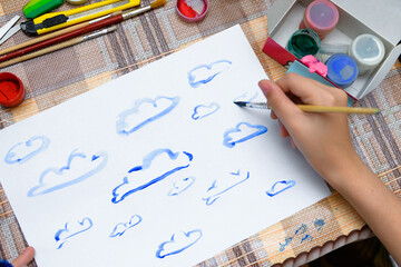 a girl drawing watercolor blue clouds on a blank white paper, artistic creation at home, makes creative artwork