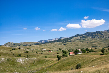 Fantastic mountain views in Montenegro. The hills are covered with grass and trees. Beautiful blue sky. Village in the hills.