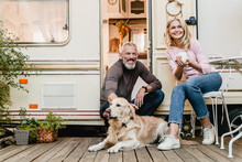 Portrait Of Senior Joyful Smiling European Couple With Their Labrador Resting In The Doorway Of Their Caravan Home
