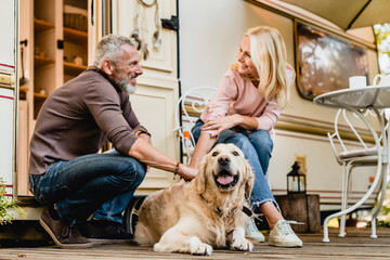 Elderly caucasian beautiful couple petting their dog together near their motorhome