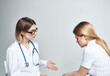 © SHOTPRIME STUDIO - Doctor sits on a chair and a woman patient indoors on a light background
