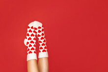 Close-up Of Women's Legs In Warm Socks With A Heart Print In A Flirty Pose On A Red Background With A Place For Text
