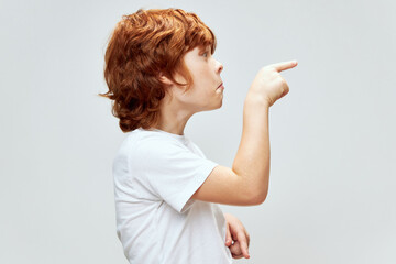 red-haired boy stands sideways points his finger to the side gray background Copy Space