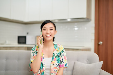 Wall Mural - Young woman in casual talking on mobile at home on the sofa.