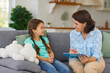 © Studio Romantic - Happy little child communicating with psychologist sitting on sofa during therapy session at home