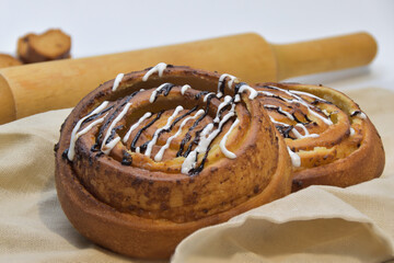 Two sweet buns with glazing on the napkin, wooden rolling pin in the background.