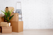 Moving Day Concept - Cardboard Boxes, Houseplants And Other Things Over White Brick Wall Background