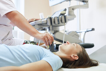 Woman patient during the ultrasound examination of a thyroid lying on the couch in medical office. Girl having neck ultrasound scanning test.