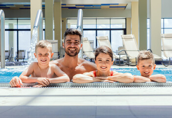 Wall Mural - smiling family of four having fun and relaxing in indoor swimming pool at hotel resort.