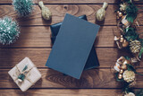 Fototapeta  - Mockup blank black book cover with Christmas gift box, Xmas ornaments and Christmas tree model decor on wooden table background. Flat lay, Top view with copy space