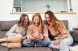 © CarlosBarquero - Group of female friends on the sofa at home, using a mobile phone laughing.