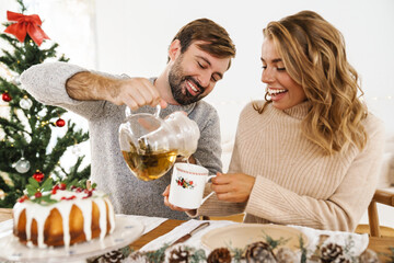 Wall Mural - Happy couple drinking tea with pie while having Christmas dinner