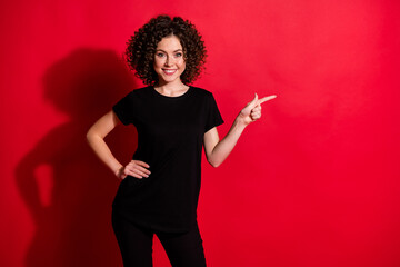 Sticker - Portrait of pretty cheery wavy-haired girl pointing forefinger aside copy space ad isolated over bright red color background