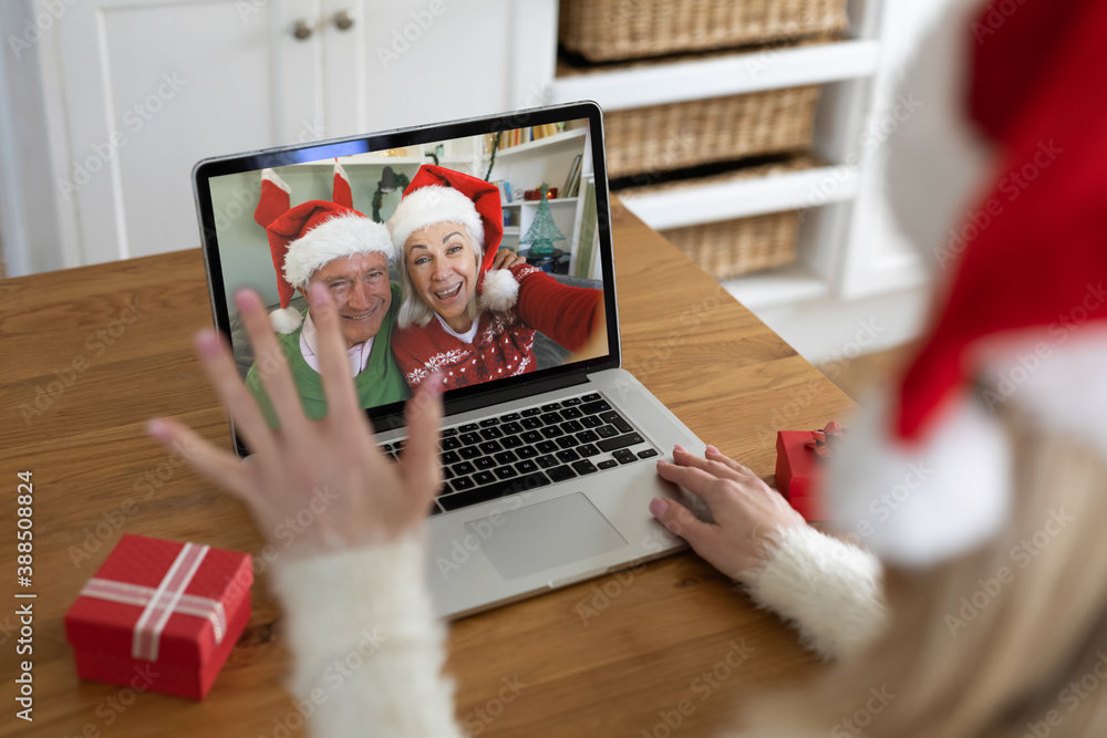 Rear view of woman in santa hat waving while having a videocall with senior couple in santa hats on  - obrazy, fototapety, plakaty 