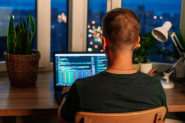 Wall Mural - a young male programmer in front of a window with a lights of night city, on his laptop screen is co