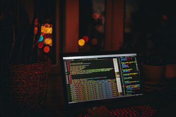 Wall Mural - a young man programmer coding on a laptop in the dark with a view of the lights of the night city, c